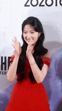 a woman in a red dress is smiling and clapping her hands .