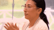 a woman wearing glasses applauds in front of the great canadian baking show