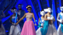 a woman in a pink dress is dancing on a stage with masked dancers