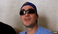 a man wearing sunglasses and a blue hat is making a face .