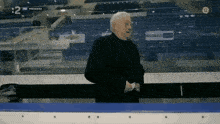 a man in a black suit is standing in a stadium with the number 12 on the bottom right corner