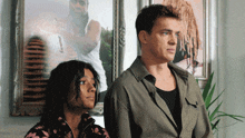 a man and a woman stand in front of a framed picture of a man with dreadlocks