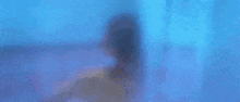 a woman without a shirt is taking a shower in front of a blue wall with a pattern on it .