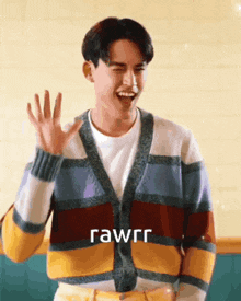 a young man wearing a striped cardigan is laughing and waving .