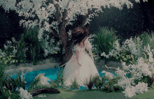 a woman in a white dress is standing under a tree