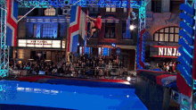 a man is jumping over a pool with a ninja sign in the background