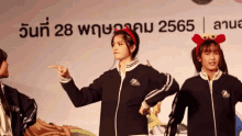three girls are dancing in front of a sign that says ' 2565 ' on it