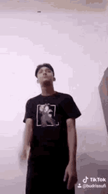 a man in a black shirt is standing in front of a wall .