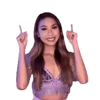 a woman in a purple top is smiling and pointing up with her fingers .