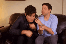 two men are sitting on a couch one is looking at a cell phone