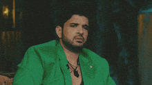 a man wearing a green jacket and a necklace with the letter g on it