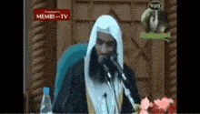 a man is speaking into a microphone in front of a sign that says memri tv .