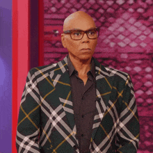 a bald man wearing glasses and a plaid jacket looks at the camera