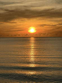 the sun is setting over the ocean with a few clouds in the sky
