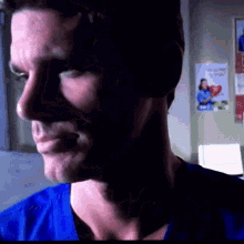 a man in a blue scrub is smiling in front of a wall with a poster that says " i love you " on it