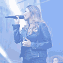 a woman in a leather jacket singing into a microphone with a blue background behind her
