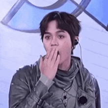a young man is covering his mouth with his hand .
