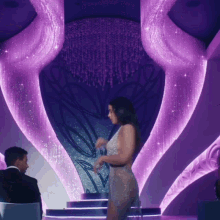 a woman in a very short dress is dancing in front of a purple chandelier