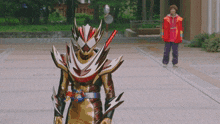 a man in a red jacket stands next to a superhero with a sword