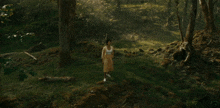 a woman in a white tank top and a yellow skirt stands in the middle of a forest
