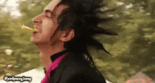 a man with a mohawk and a pink shirt is eating a slice of pizza .