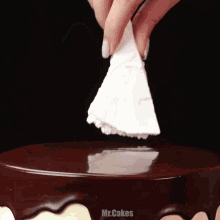 a person is holding a piece of white frosting over a chocolate cake that says mr.cakes on it