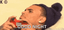 a man in a beanie is holding a video game controller in his mouth and saying `` good night '' .