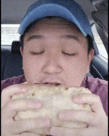 a man in a blue hat is eating a sandwich with his eyes closed