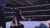 a woman is kneeling down in a wrestling ring while a referee stands nearby