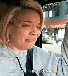a woman is crying in a car while holding a piece of bread and says `` lets get this bread '' .