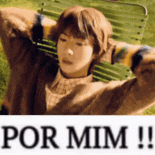 a young boy is sitting on a park bench with his arms outstretched and a sticker that says por mim .