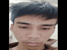 a close up of a young man 's face with a brown shirt on