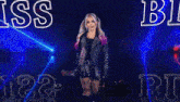 a woman in a leather jacket is standing in front of a stage with the name alexa bliss written on it .