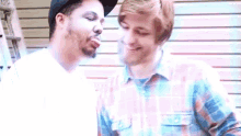two men are standing next to each other and one of them is blowing a kiss on the other 's cheek .
