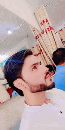 a man with a beard wearing a white shirt looks up at something