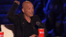 a bald man is sitting in front of a microphone and holding a red cup .