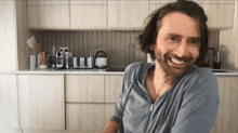 a man with long hair and a beard smiles in front of a kitchen counter