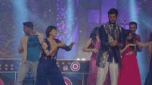a group of people are dancing on a stage in front of a purple background