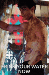a shirtless man with a tattoo on his chest is standing in front of a window with the words drink your water now below him