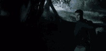 a man is standing in the dark in a forest holding a tree branch .