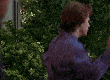 a young man in a blue shirt is standing in front of a tree
