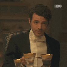 a man in a tuxedo and bow tie is sitting at a table holding a martini glass .