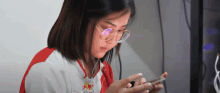 a girl wearing glasses and a red bull shirt looks at her phone