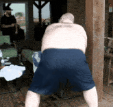a shirtless man in blue shorts is standing on a porch