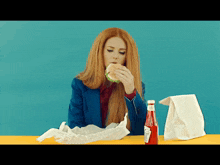 a woman is eating a hamburger next to a bottle of ketchup