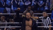 a wrestler stands in a ring with a referee and a crowd behind him with a shirt that says stan on it