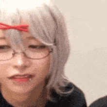 a woman wearing glasses and a wig with a red bow on her forehead .