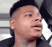 a man with a tattoo on his neck is sitting in a car making a funny face .