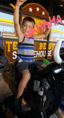 a young boy riding a bull in front of a texas best steakhouse