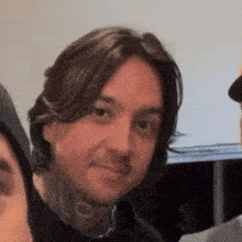 a man with long hair and a tattoo on his neck is smiling
